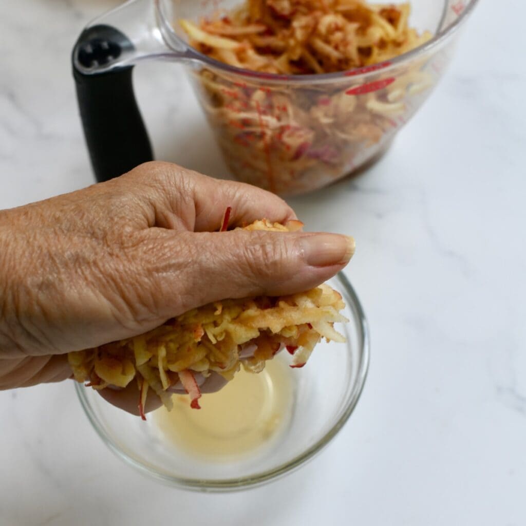 Hand squeezing out the excess moisture from shredded apple.