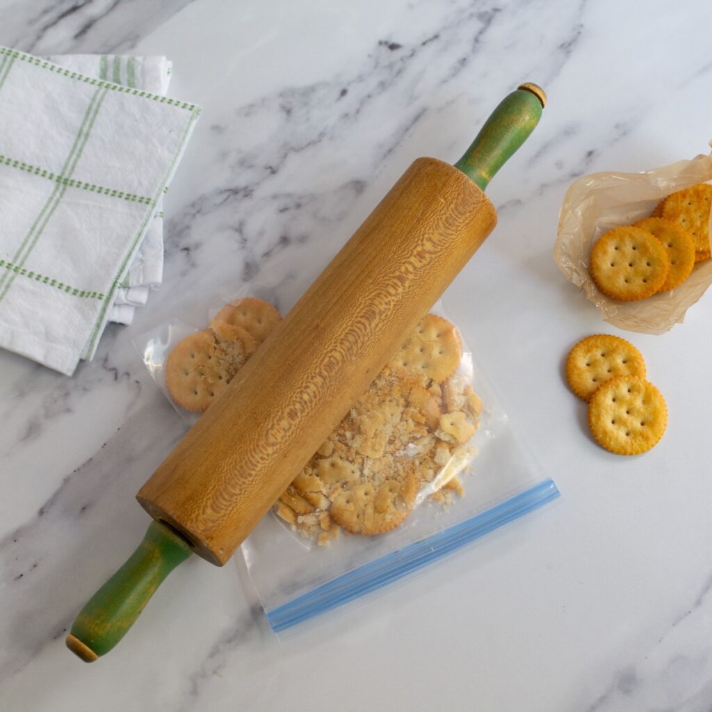 Using a rolling pie to crush the ritz crackers in a bag.