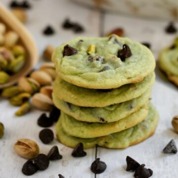 Stack of chocolate chip pistachio cookies on a wooden surface.