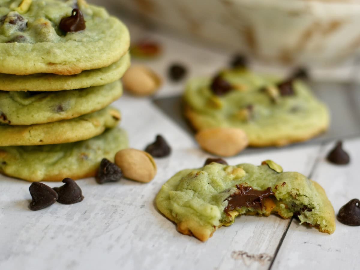 Chocolate chip pistachio cookies stacked on top of each other with one next to the stack with a bite taken.