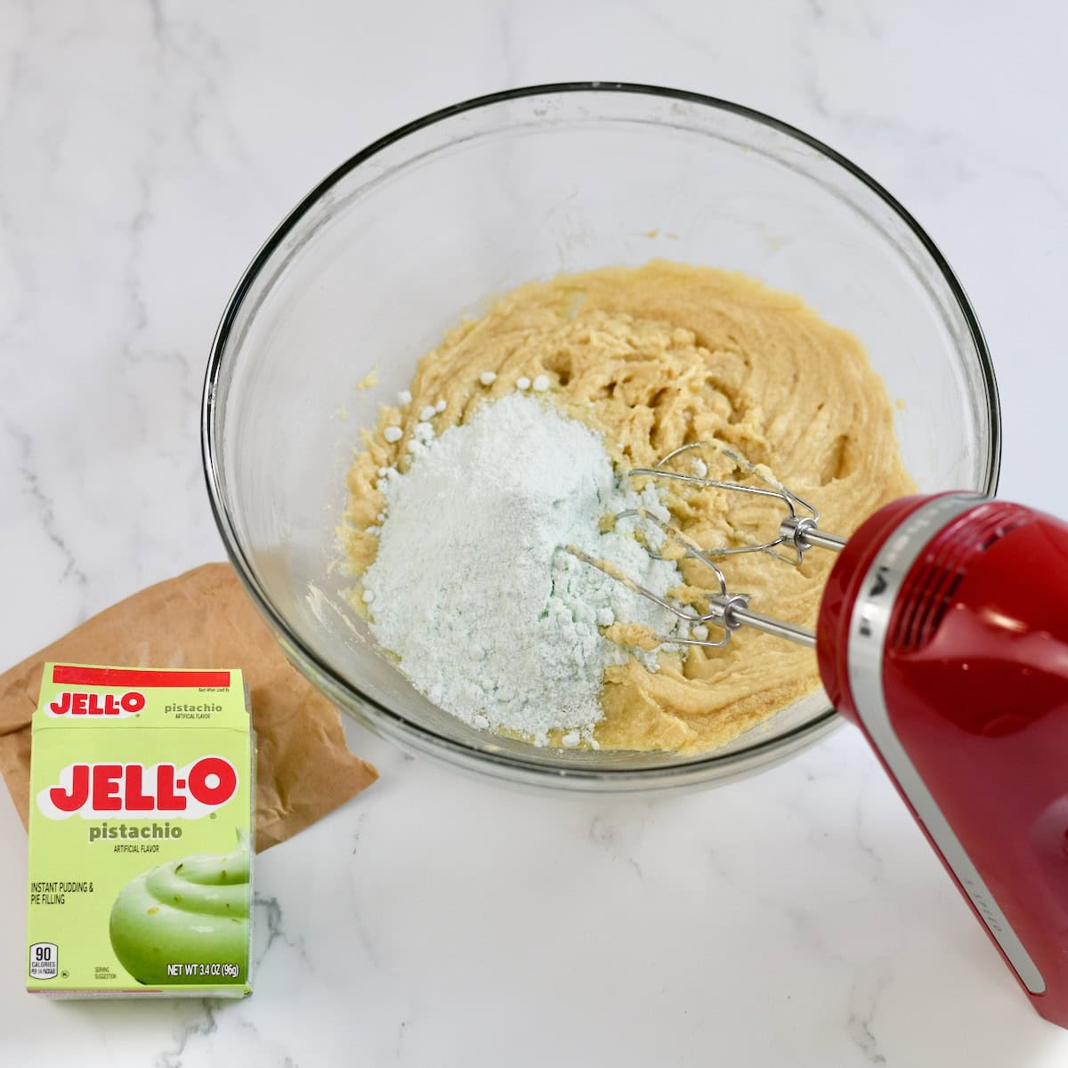Adding pistachio jello to the cookie dough in a mixing bowl.