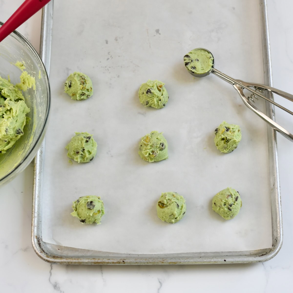 Scooping the chocolate chip pistachio cookies onto a parchment lined sheet pan.