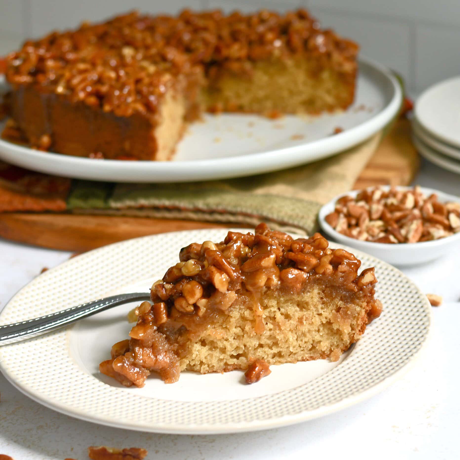 Slice of pecan upside down cake on a plate with more cake in the background.