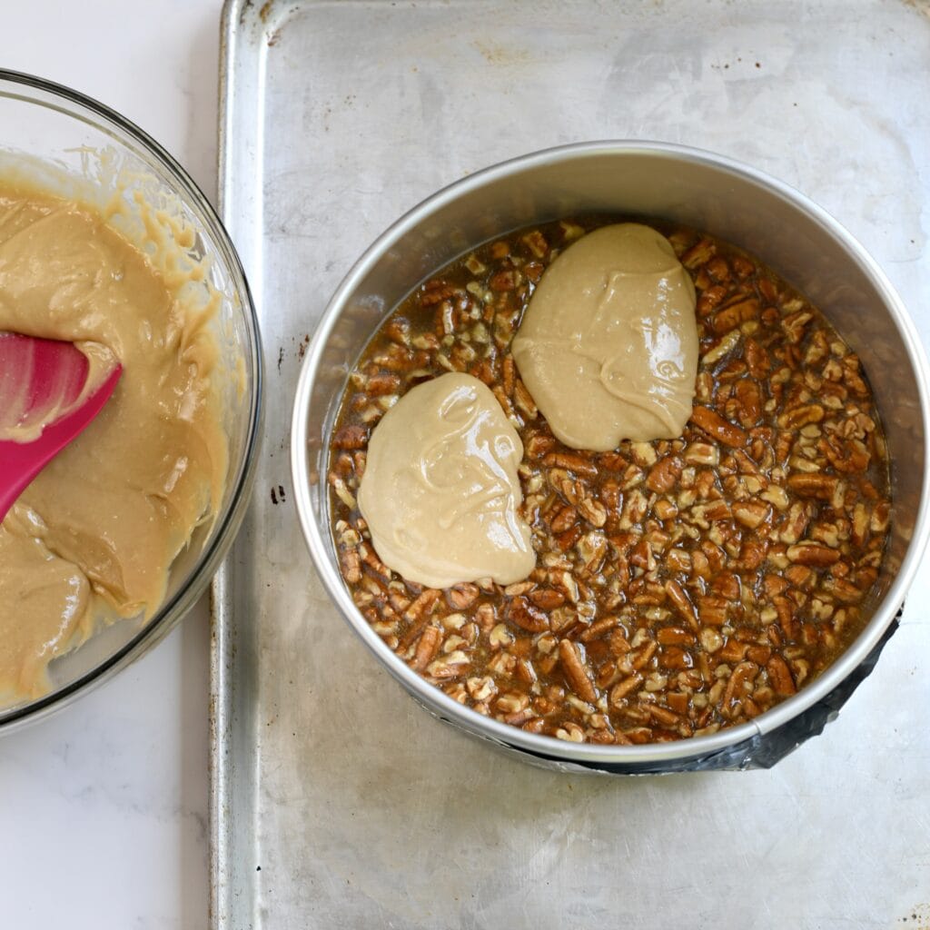 Scooping cake batter on top of the pecan layer in a cake pan.