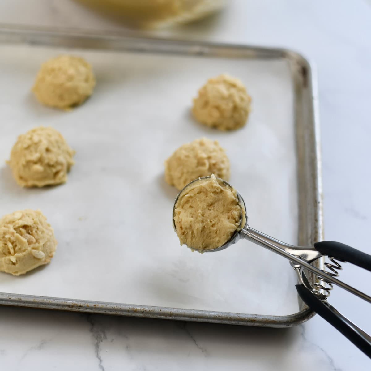 Scooping the rice krispie cookie dough onto a sheet pan.