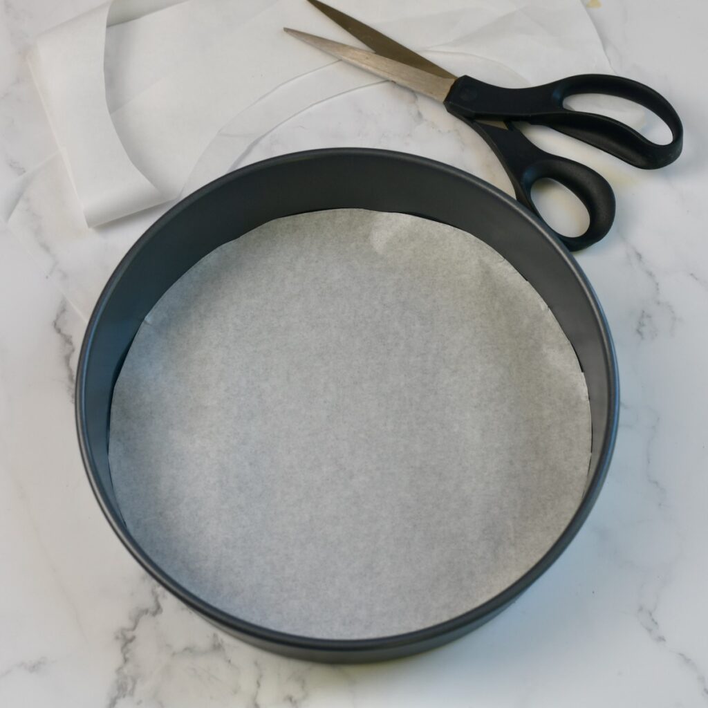 Round cake pan with parchment paper circle in bottom and scissors next to it.
