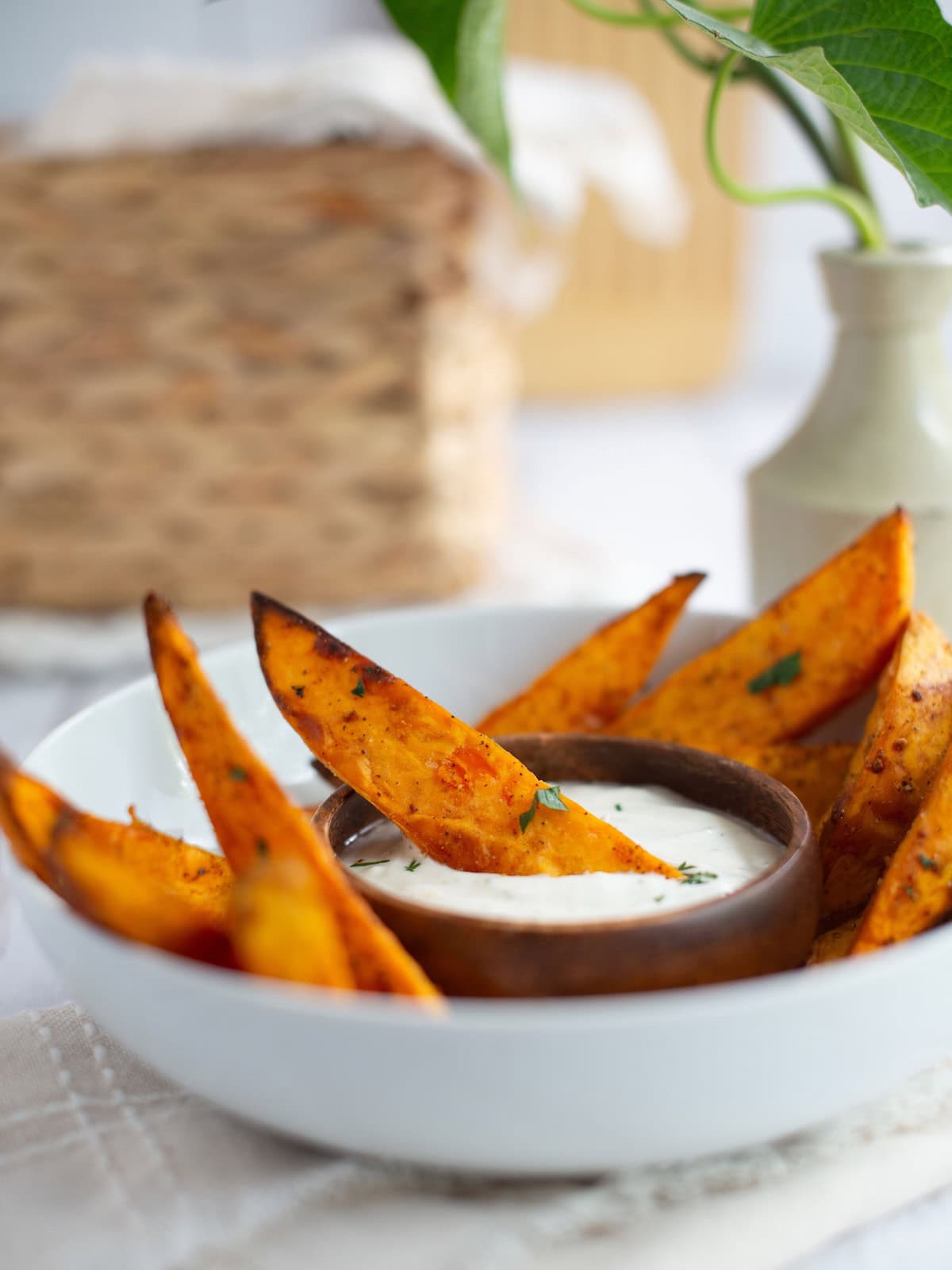 Sweet potato wedges in a bowl with one dipped in sauce in the middle.