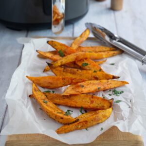 Crispy air fryer sweet potato wedges served on a parchment lined wooden board.