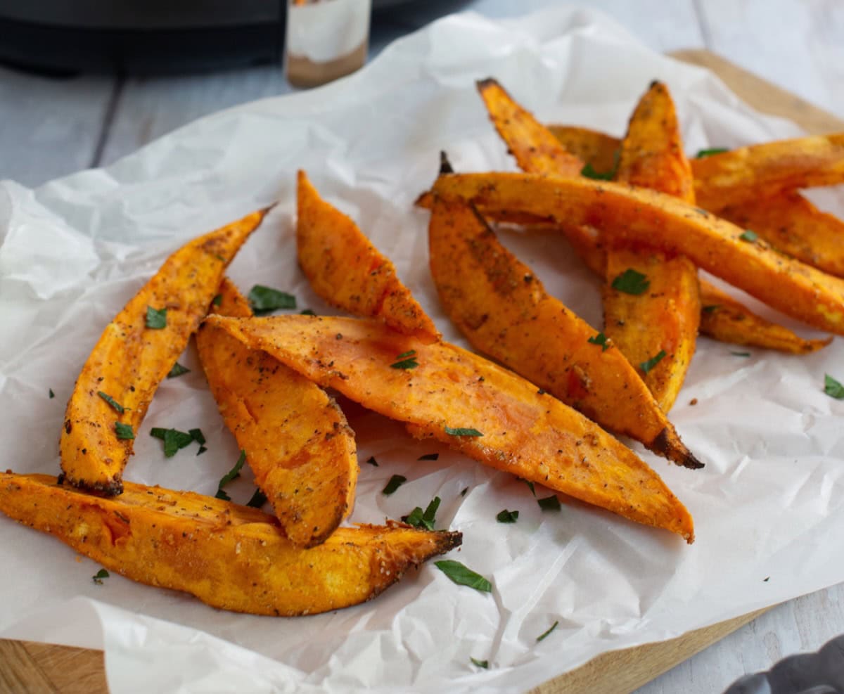 Close up of air fryer sweet potato wedges on a parchment lined wooden board.