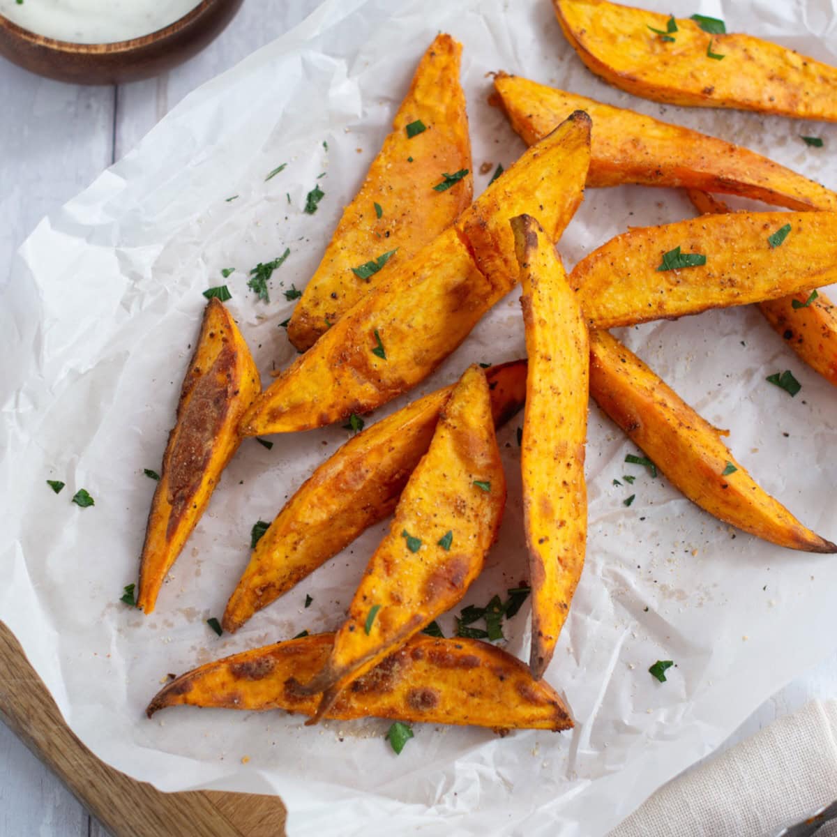 Air fryer sweet potato wedges on a parchment paper next to a ramekin of sauce.