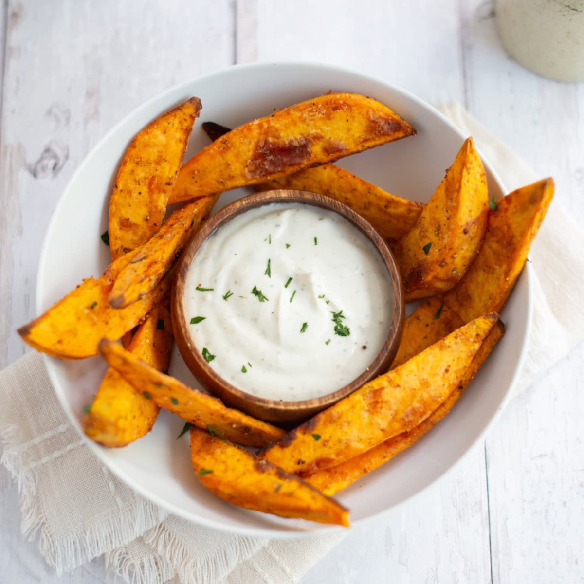 Overhead shot of air fryer sweet potato wedges in a bowl around a ramekin of sauce.