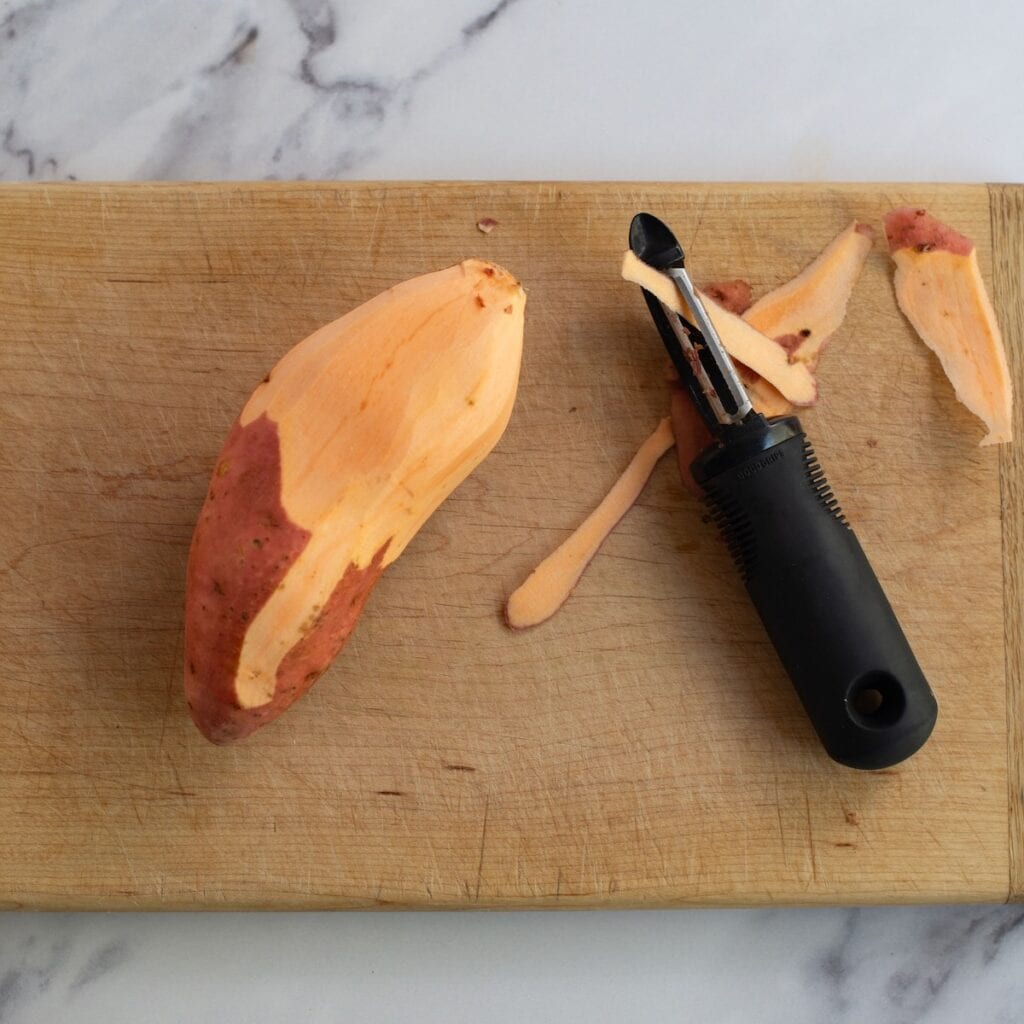 Peeling a sweet potato on a wooden cutting board.