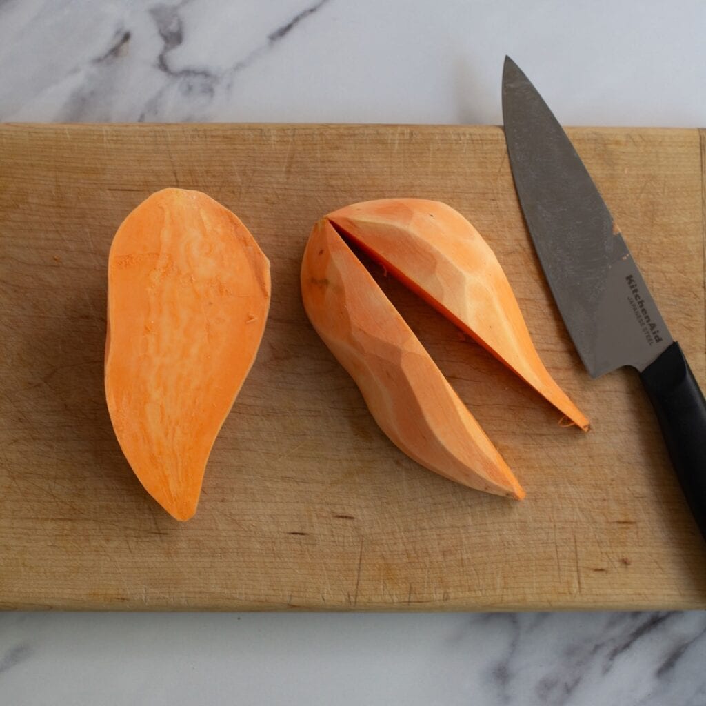 A sweet potato cut in half and one half but into quarters on a wooden cutting board.