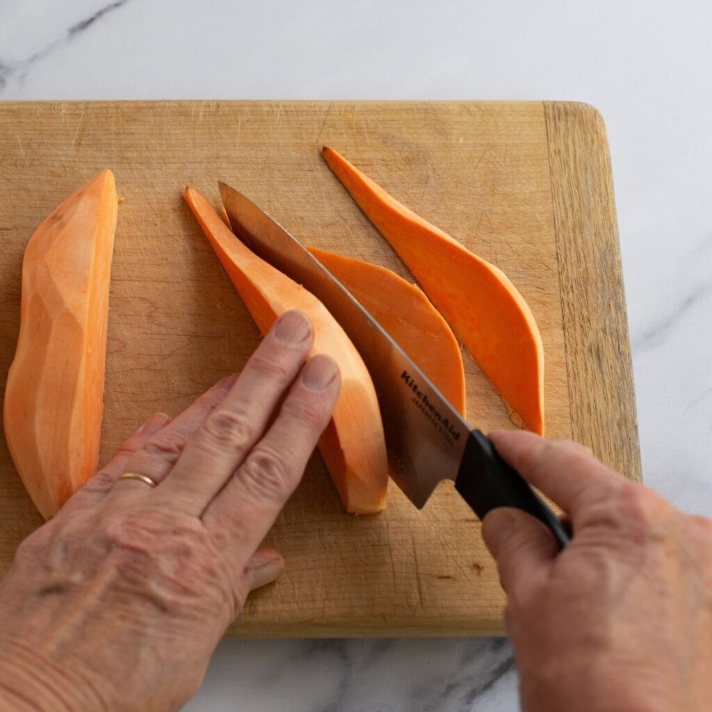 Hands slicing a sweet potato into wedges.