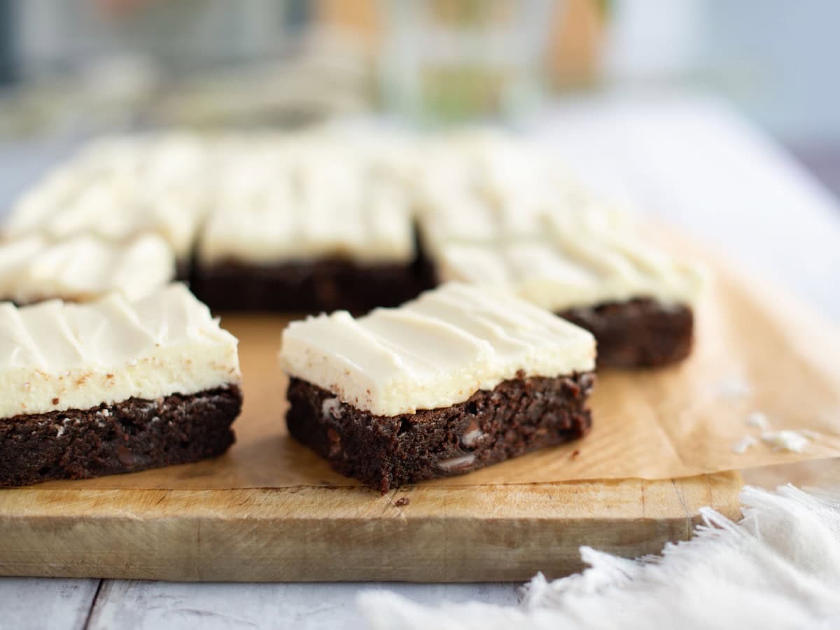 Side view of brownies with cream cheese frosting on a wooden board.