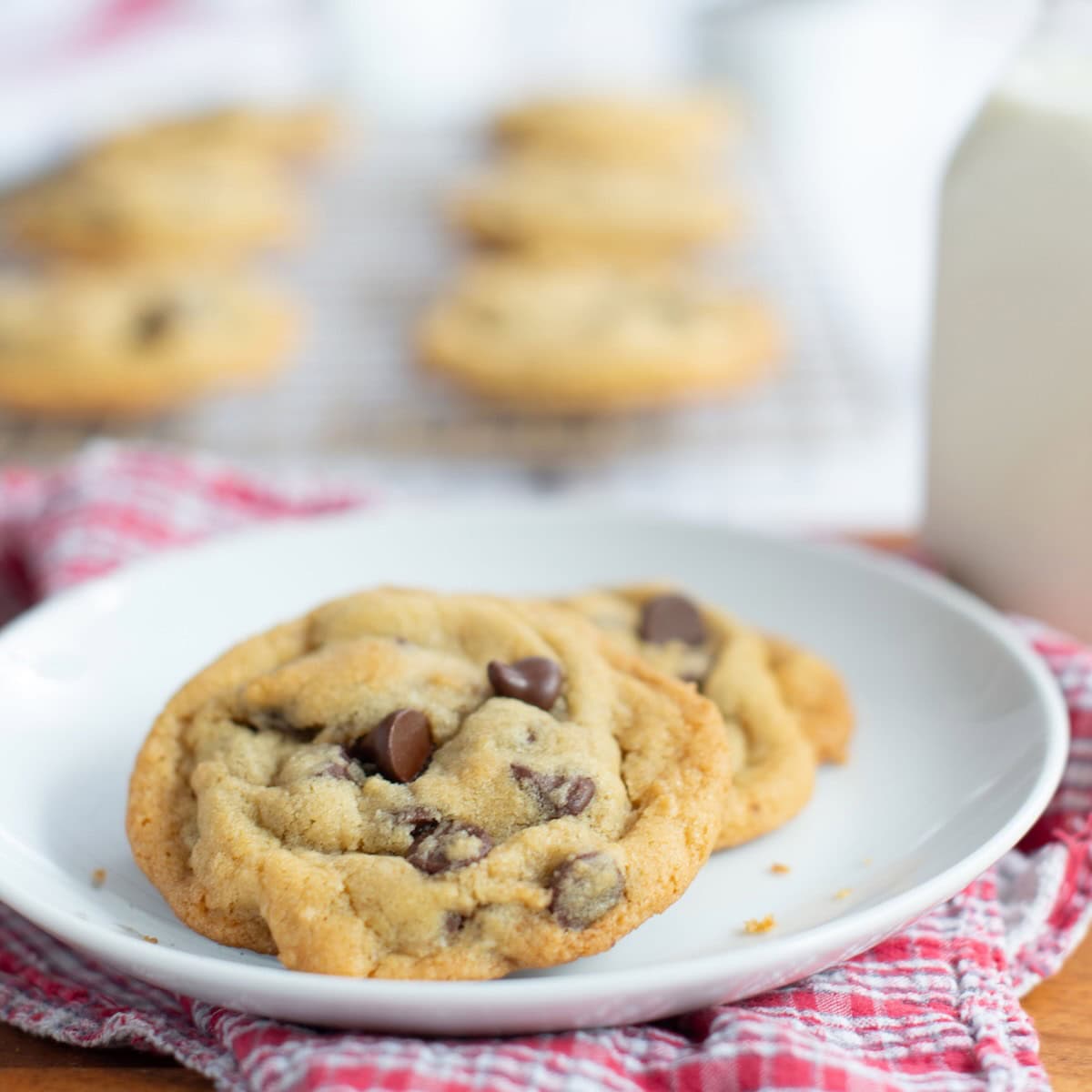 Two small batch chocolate chip cookies served on a plate with a glass of milk in the background.