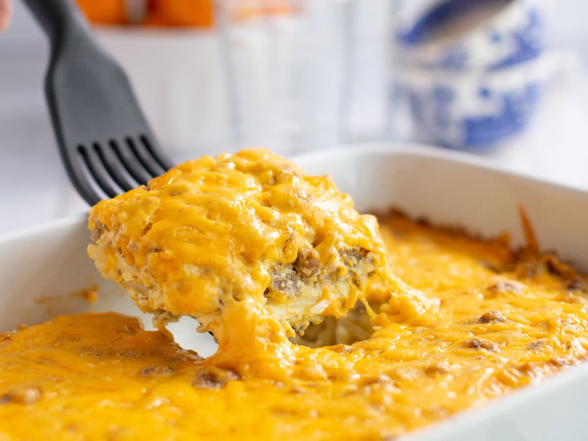 Spatula taking a portion of sausage hashbrown breakfast casserole from a baking dish.