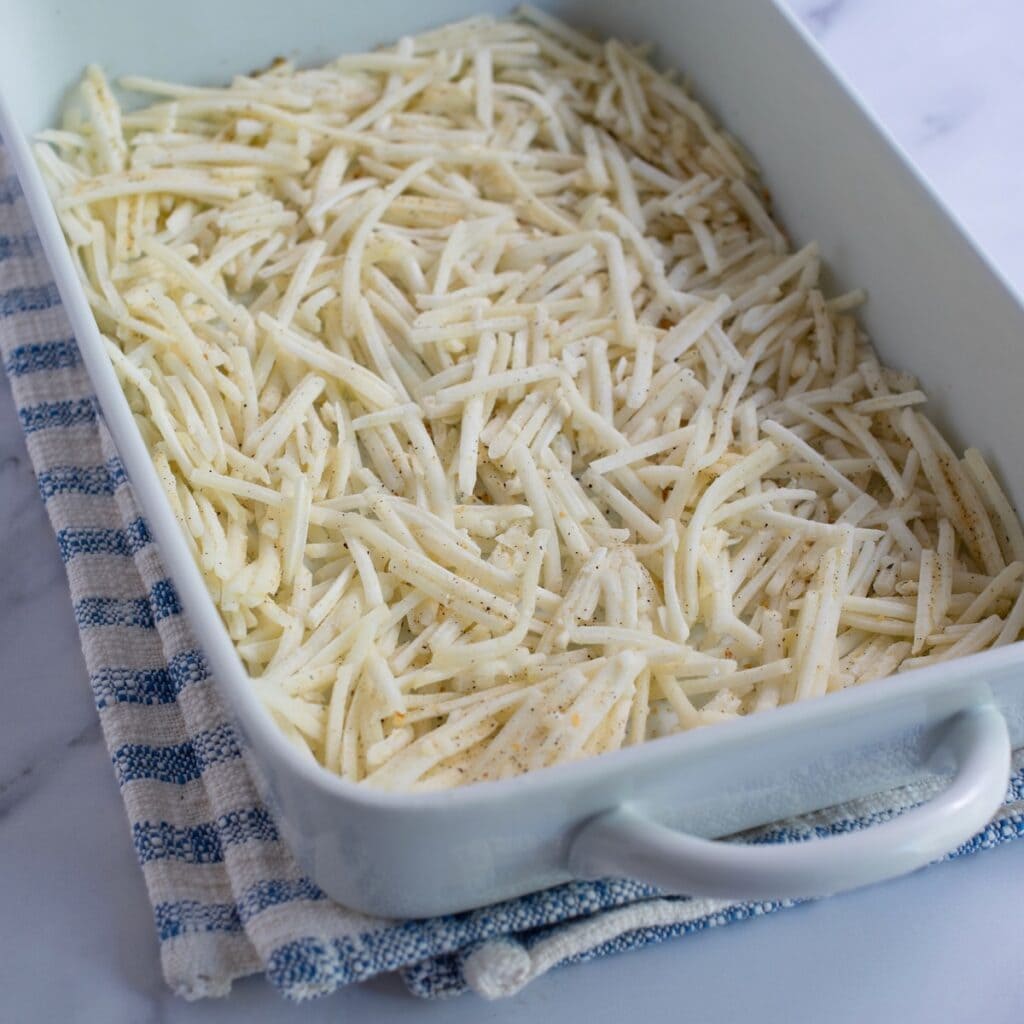 Shredded hashbrowns placed in the bottom of a white baking dish.