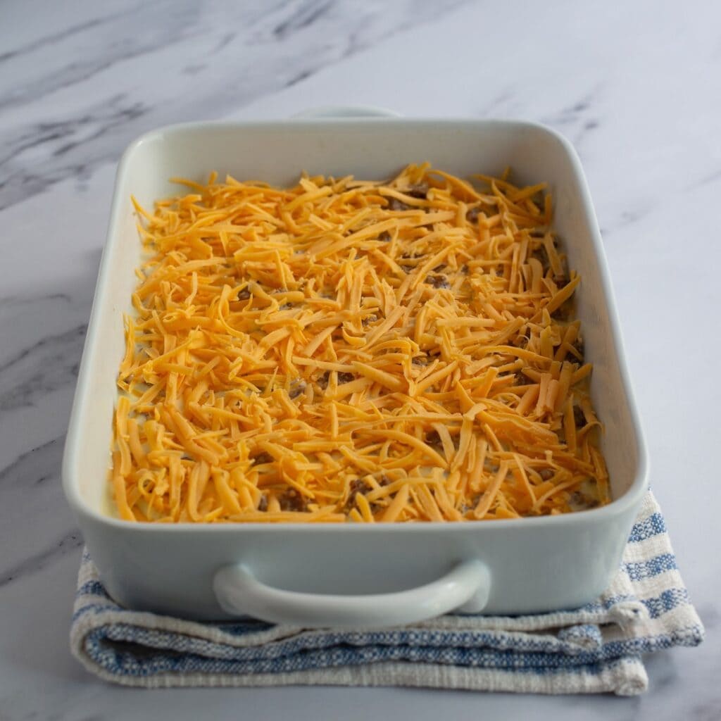 Sausage and hashbrown breakfast casserole with cheese spread on top before baking.