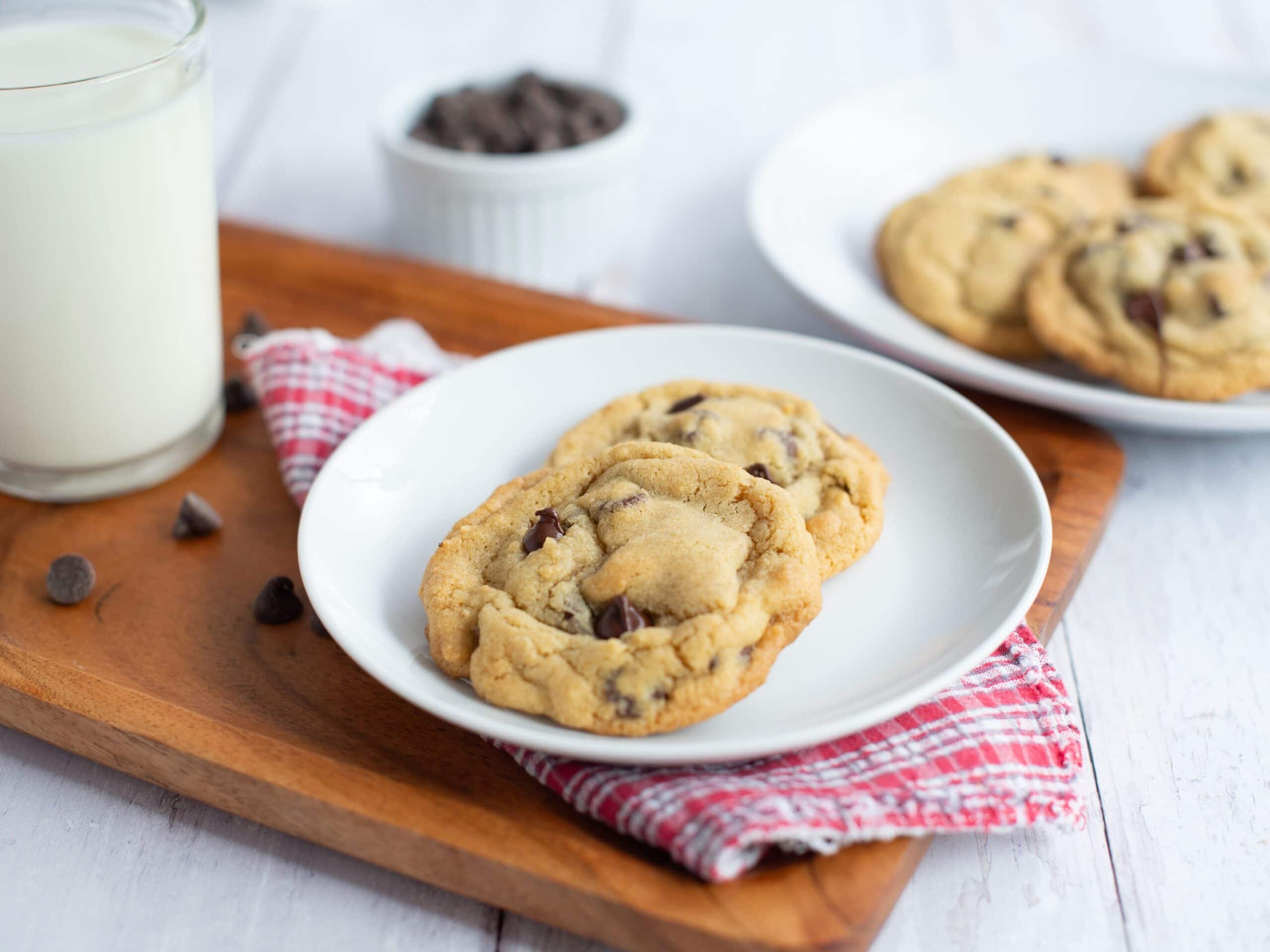 Two small batch chocolate chip cookies placed on a plate next to a glass of milk.