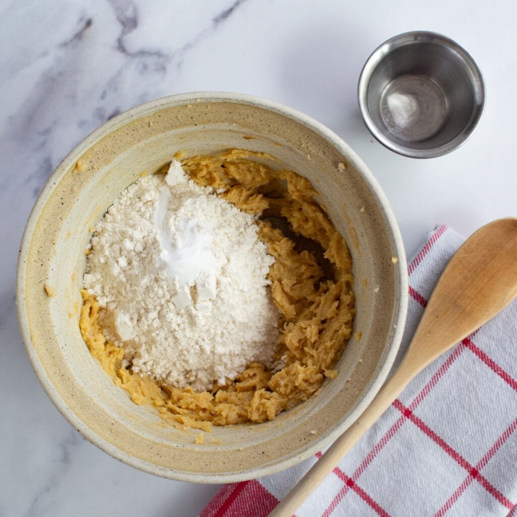 Adding dry ingredients to the butter and sugar mixture in a bowl.